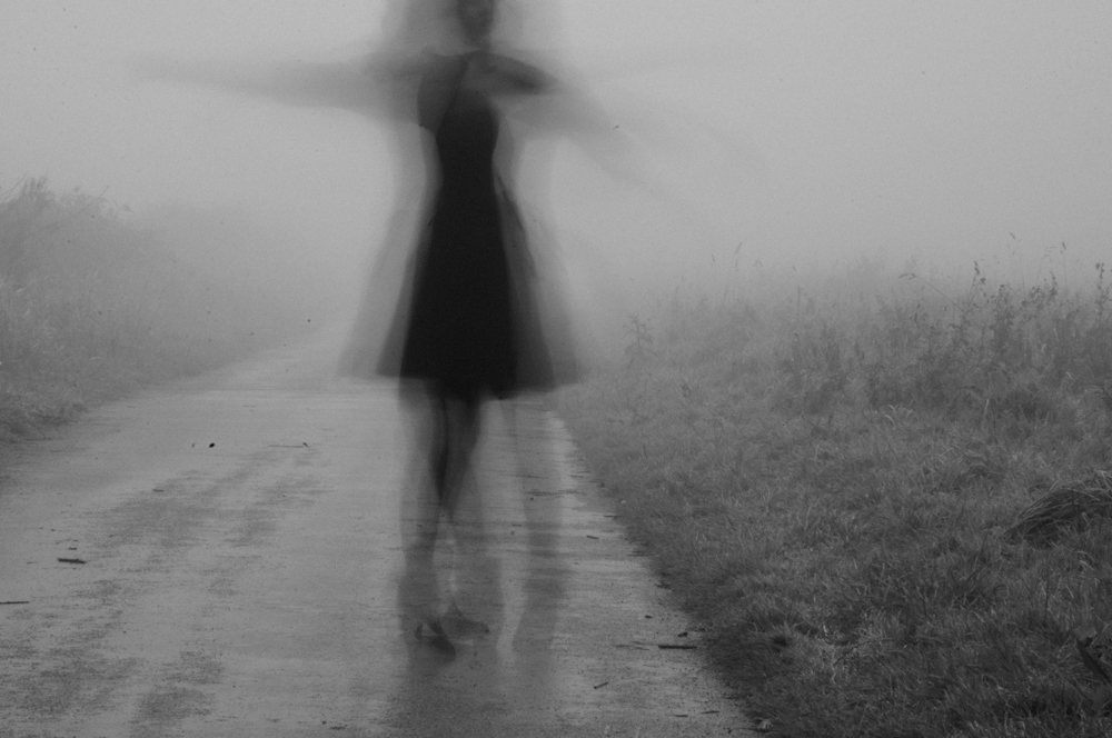 A blurred figure moving along a misty country road