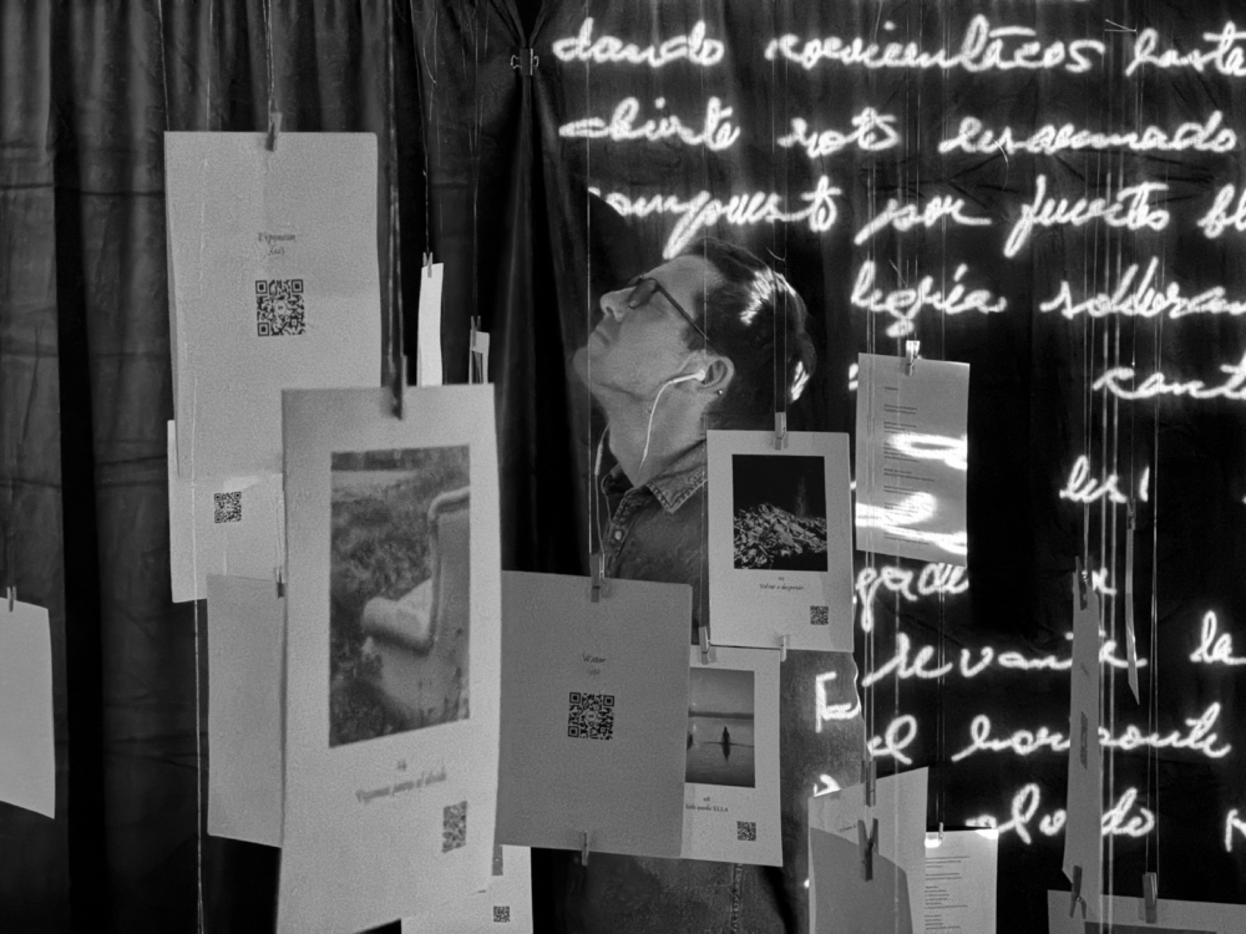 A visitor listening among suspended photographs and projected words
